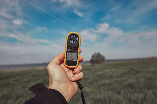 Person holding modern digital anemometer outdoors for measuring wind speed, temperature, humidity and other atmospheric effects.