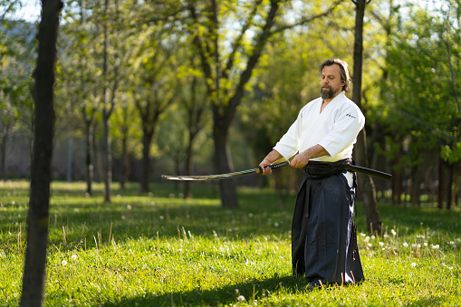 Aikido sensei in hakama practicing with samurai sword outdoors in the park