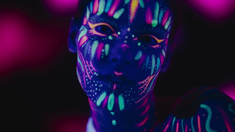 Expressive Portrait: Beautiful Young Woman with Neon Body Paint Engages the Camera, Transmitting a Sense of Mystery and Captivation Through Her Intense Gaze and Striking Appearance