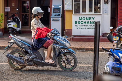 Luang Prabang, Laos - March 17th 2023: Young woman driving on a motorbike driving down the main street