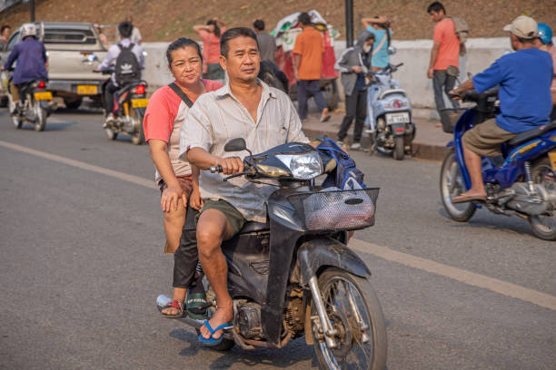 Luang Prabang, Laos - March 21th 2023: Middle aged couple on a motorbike driving down the main street towards the setting sun