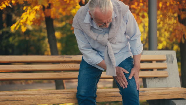 Senior man feeling strong knee pain while standing up from a bench, arthritis