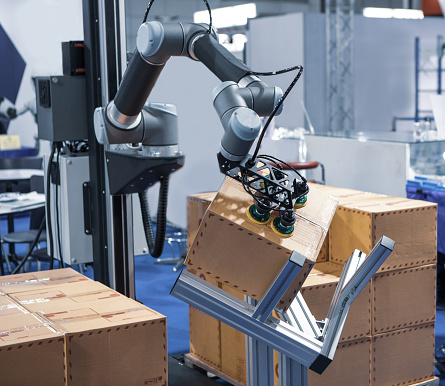 Robot arm handling carton from pallet in modern warehouse.