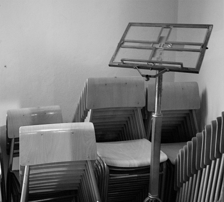 evocative black and white textured image of stacked chairs with a lectern next to them
