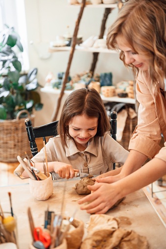 Creating the shape by using clay. Mother with little girl doing pottery at home.