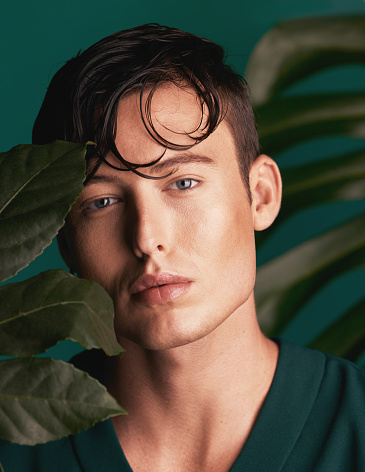 Gen z, man and portrait of a calm model with relax face and fashion aesthetic. Isolated, green background and studio of a young person with Monstera plants for organic skincare and eco friendly style