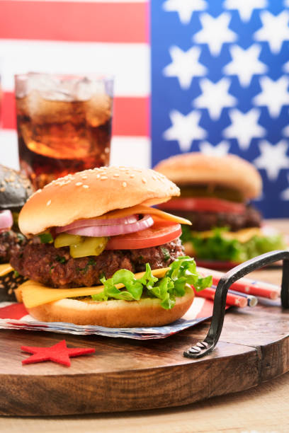4th of July American Independence Day traditional picnic food. American Burger and cocktail, American flags and symbols of USA Patriotic picnic holiday on white wooden background. Top view 4 de julio día de la independencia de los estados unidos comida tradicional tipo picnic. hamburguesa americana y cóctel, banderas estadounidenses y símbolos de vacaciones de picnic patrióticas de ee. uu. sobre fondo de madera blanca. vista superior
