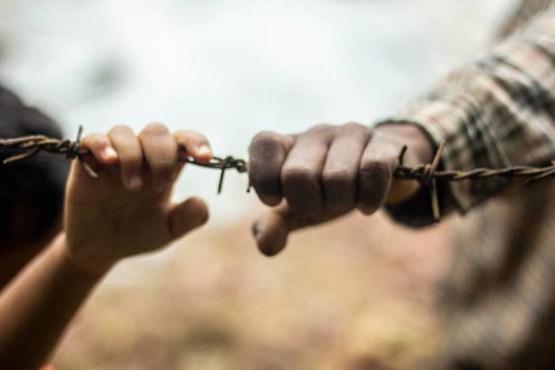 Two boys are holding 'barbed wire' with their hands and the background behind its blur