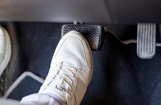 Pair of white sneakers on the floor in a car pressing brake against gas, carefully driving car concept