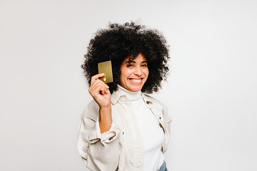 Cheerful young woman smiling at the camera while holding a credit card in her hand. Happy woman with curly hair recommending electronic banking and online shopping.
