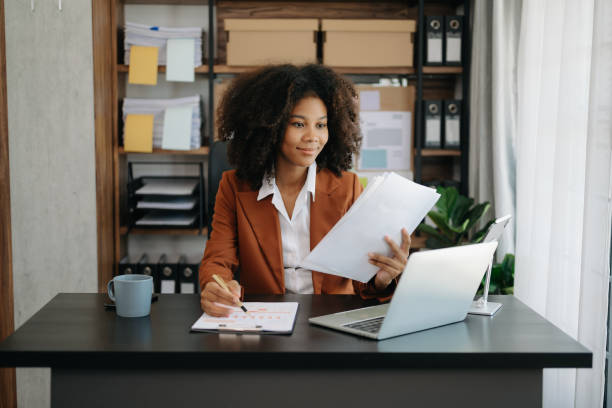 istock Confident beautiful African businesswoman typing laptop computer and digital tablet while holding coffee at office 1492884977