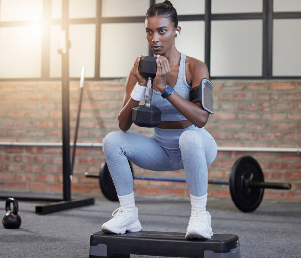 Woman, fitness and weightlifting dumbbells in squat at gym for intense exercise, workout or strength training. Serious female lifting weights and exercising for healthy wellness or bodybuilding mancuernas de mujer, fitness y levantamiento de pesas en sentadilla en el gimnasio para ejercicio intenso, entrenamiento o entrenamiento de fuerza. levantamiento de pesas femeninas serias y ejercicio para un bienestar saludable o culturismo