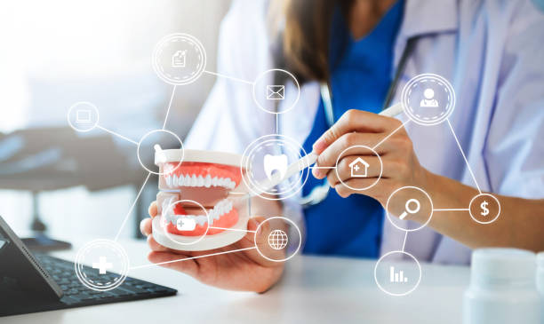 dentista concentrato seduto a tavola con campioni di mascella modello di dente e lavorando con tablet e laptop in studio dentistico professionale clinica dentale. medico che lavora con il diagramma dell'icona vr - usare la bocca foto e immagini stock