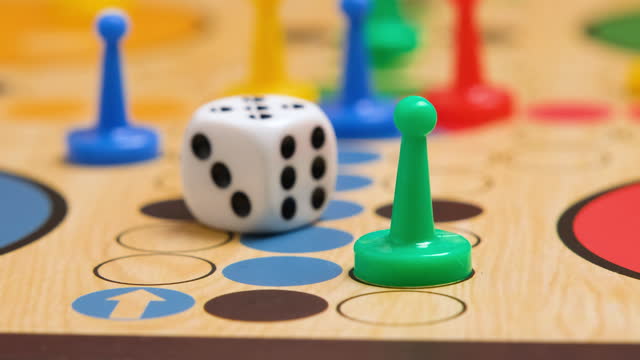 People play Ludo or Pachisi board game on beautiful wooden play board. Ludo is a strategy board game for two to four players. 4K resolution family board game video.