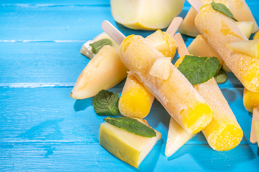 Melon ice cream popsicle, sweet sorbet lollypops, homemade gelato on sticks, with slices of fresh cantalupa melon and mint leaves