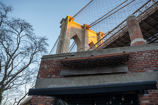 Low angle of Brooklyn Bridge peaking over old brick building, Bridge Park, Dumbo Brooklyn.