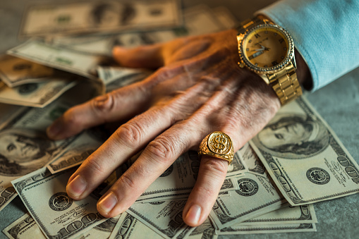 A man wearing gold watch and ring with US dollars