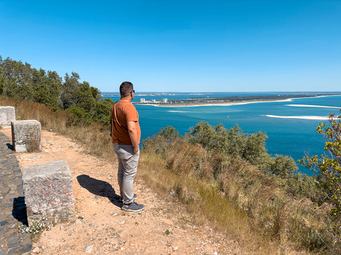Absorbed man traveling alone, carrying a backpack, looking into the distance, watching horizon, enjoying the view of beautiful nature with splashing waves on the headland, standing alone on the cliff