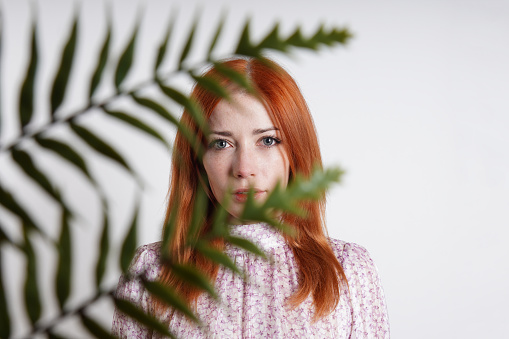 indoor portrait of mid adult woman hiding behind house plant palm leaves