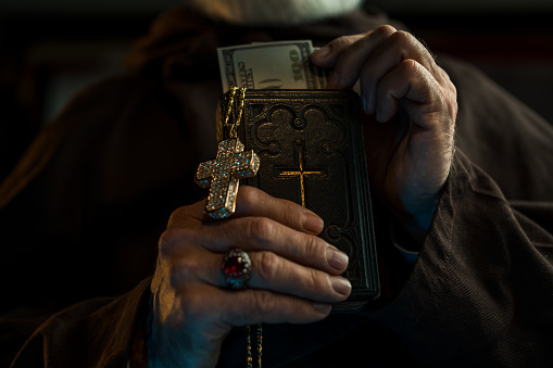 Priest holding Holy Bible and US dollars