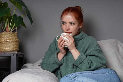 woman in turleneck sweater relaxing at home drinking coffee and daydreaming