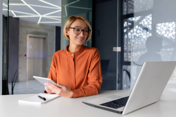 istock Young female manager, office worker sits at the table and talks via video connection from a laptop, participates in an online conference and business meeting, writes in a notebook 1492896525