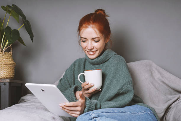 woman relaxing at home using tablet computer for entertainment or communication and drinking coffee