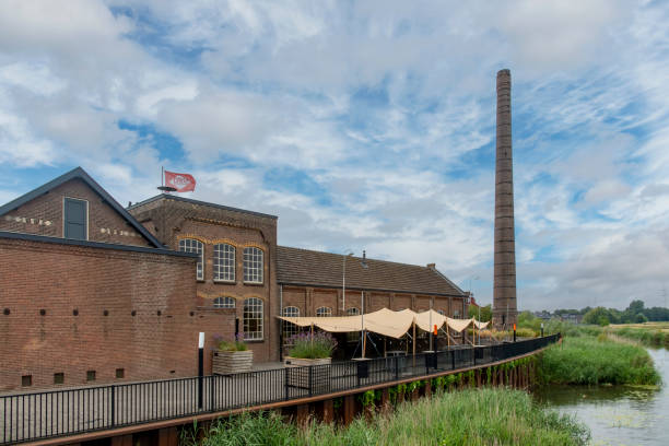 Ulft, the Netherlands-August 2022; Side view of DRU Culture Factory, a refurbished old iron-casting factory with remaining old architectural details like the high chimney along the Oude IJssel River