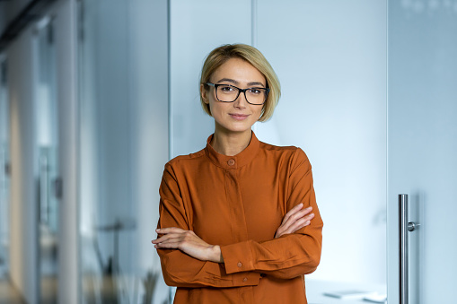 Portrait of a young beautiful woman designer, architect, programmer standing in the office with her arms crossed on her chest. Confidently and smilingly looking at the camera