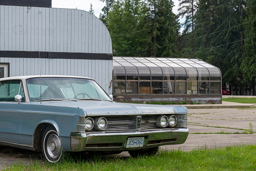 Sicamouse, BC, Canada-August 2022; View of the terrain and building of a now closed and dilapidated diner with a classic Chrysler New Yorker parked in front