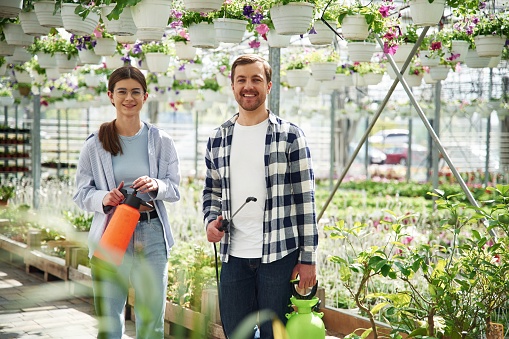 Front view. Florist man and woman are working together in bright greenhouse.