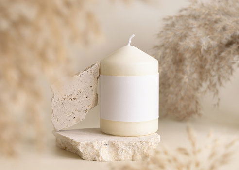 Candle with blank paper label on beige stone near dried pampas grass Close up, copy space. Boho brand packaging mock up. Home decoration, Close to nature or scandinavian style