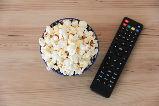 White fried air popcorn in a plate and  remote control for the TV on a brown background