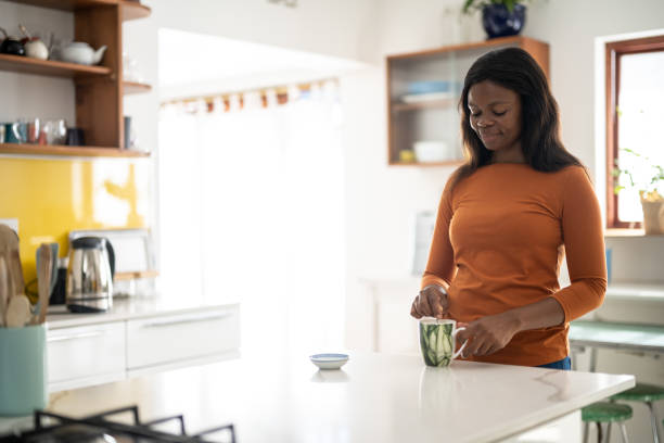 Content woman standing at the worktop counter in her kitchen stirring a freshly made hot drink in a mug