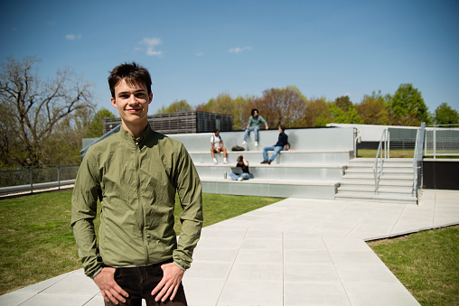 Portrait of college student on a rooftop outdoors in springtime. White young man with short hair, dressed in casual clothes. Small group of students sitting in stairs in the background. Horizontal waist up outdoors shot with copy space. This was taken in Quebec, Canada.