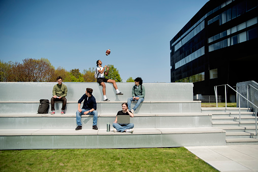Group of college students relaxing outdoors on building rooftop. Multiracial group of five young man and one young woman. They are all dressed in casual clothes. Horizontal full length outdoors shot with copy space. This was taken in Quebec, Canada.
