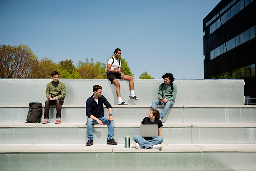 Group of college students relaxing outdoors on building rooftop. Multiracial group of five young man and one young woman. They are all dressed in casual clothes. Horizontal full length outdoors shot with copy space. This was taken in Quebec, Canada.