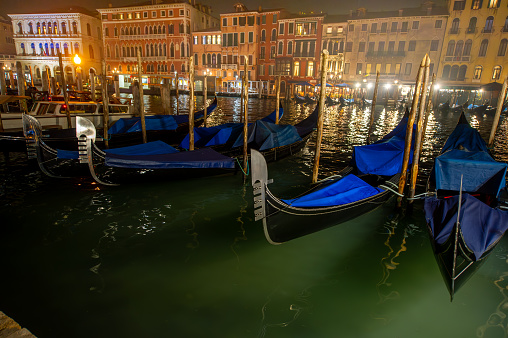 The gondola, a traditional Venetian boat, is an emblem of Venice's romantic allure. Two gondolas driven through the narrow and beautiful canals of Venice with its green water and colourful houses