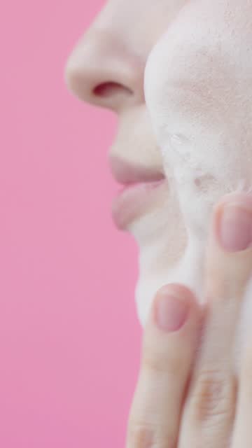 Young lady washes her face with face foam Slow motion Pink background