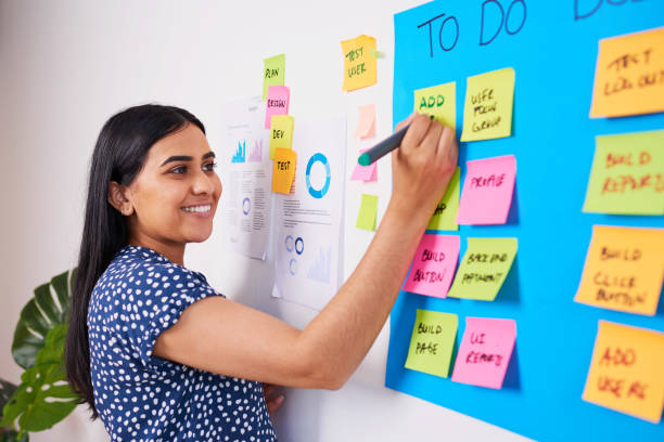 Indian woman writes ticket in backlog of colourful scrum board, KANBAN coding stock photo