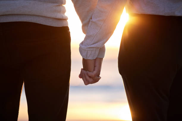 praia, casal e de mãos dadas ao pôr do sol por amor e confiança ou compromisso e apoio nas férias. mão de homem e mulher juntos em férias no mar para relaxar, viajar e se conectar na natureza com cuidado - trust human hand sea of hands holding - fotografias e filmes do acervo