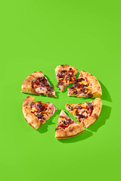 istock American pizza with thick crust, loaded with sausage, bacon, and marbled beef on a green background with sun shadows. The pizza is sliced into pieces, side view 1492929008