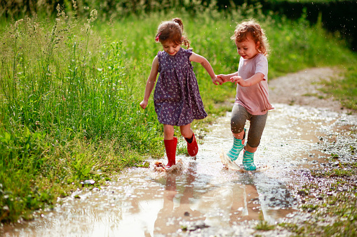 Girls walking, running and jumping on mud puddles in their rubber boots.