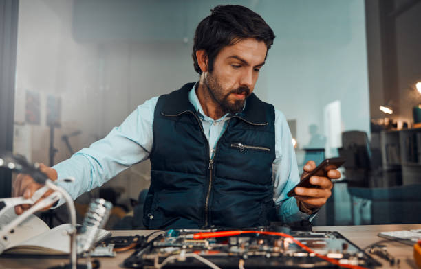 istock Computer hardware repair, phone and it worker watch a diy video to fix a semiconductor and circuit. Engineering, workshop and electric work of a male engineer with a mobile doing electrical project 1492929726