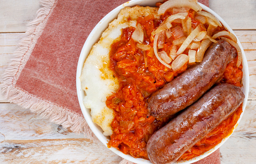 Traditional South African Pap and Wors, sausage with popular maize meal staple covered with Chakalaka or relish on wood with traditional African printed fabric