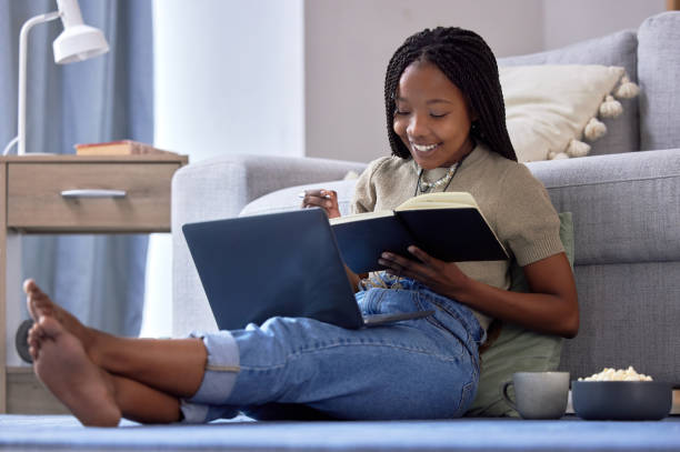 istock Student, writing and black woman with book in home living room for elearning, studying and knowledge. Laptop, education and smile of happy female with notebook for notes, information and research. 1492939990