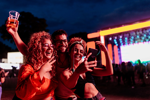 A group of three young Caucasian friends are at a concert at night having a great time and taking a selfie to document it.
