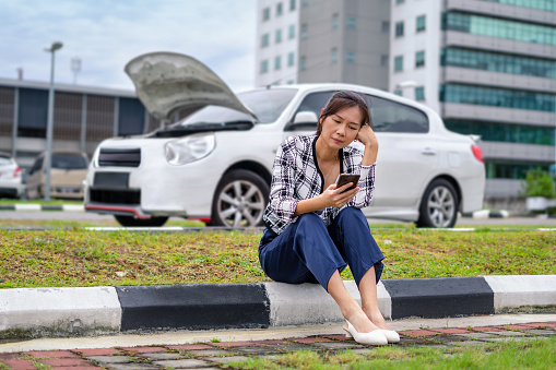 Worried Woman sitting on the side of the road with broken down car, waiting for assistance