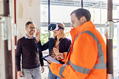 Engineer showing construction design to a couple on virtual reality glasses at building site