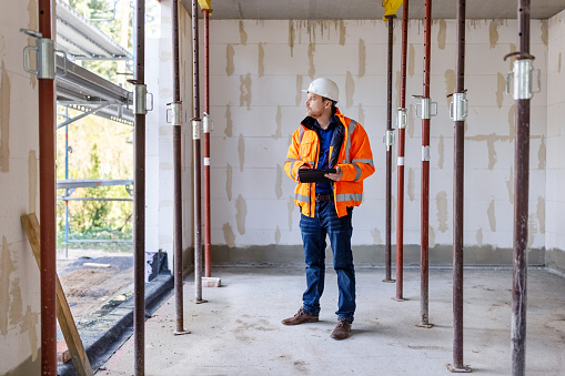 Full length shot of a construction engineer working at construction site. Male architect holding digital tablet standing at under construction building site.